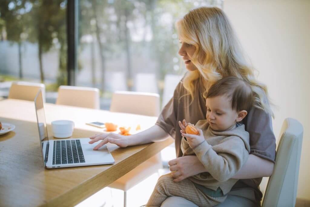 A woman sitting and holding a child in front of the laptop