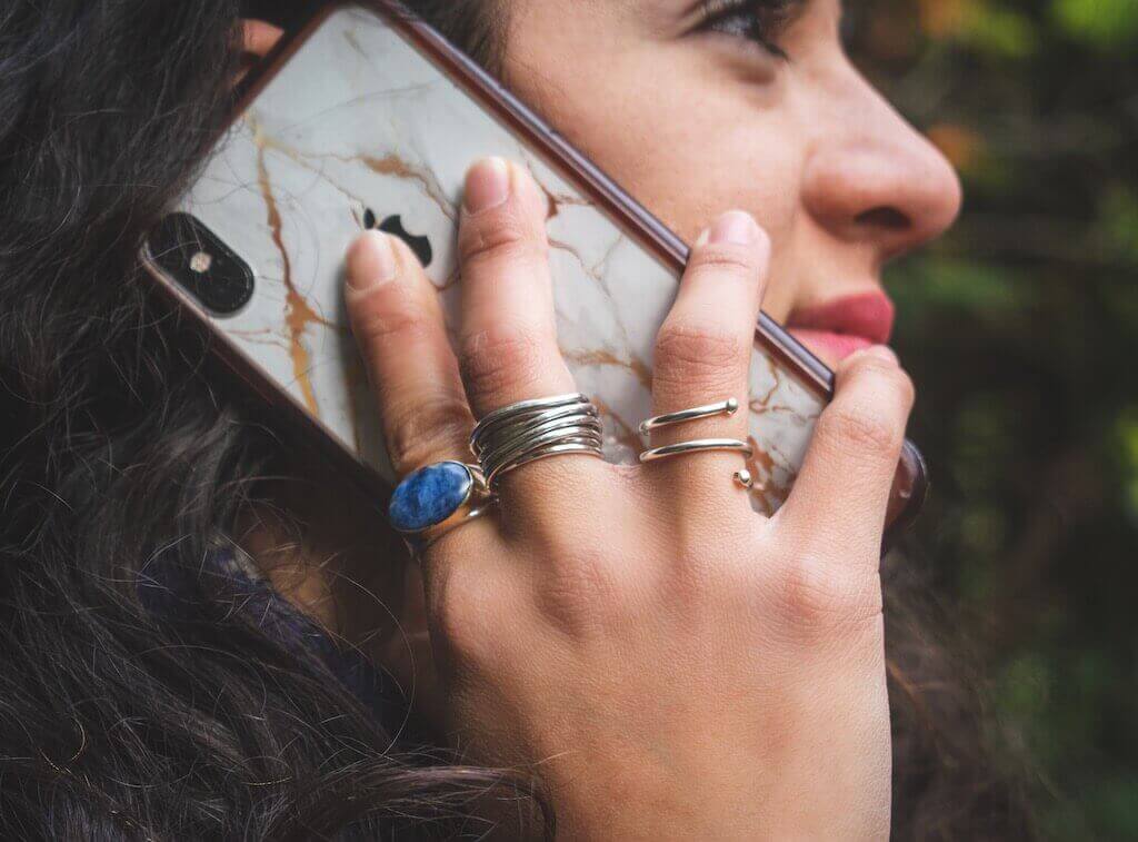 A woman with silver rings, holding an iPhone with a white mask, and talking to someone