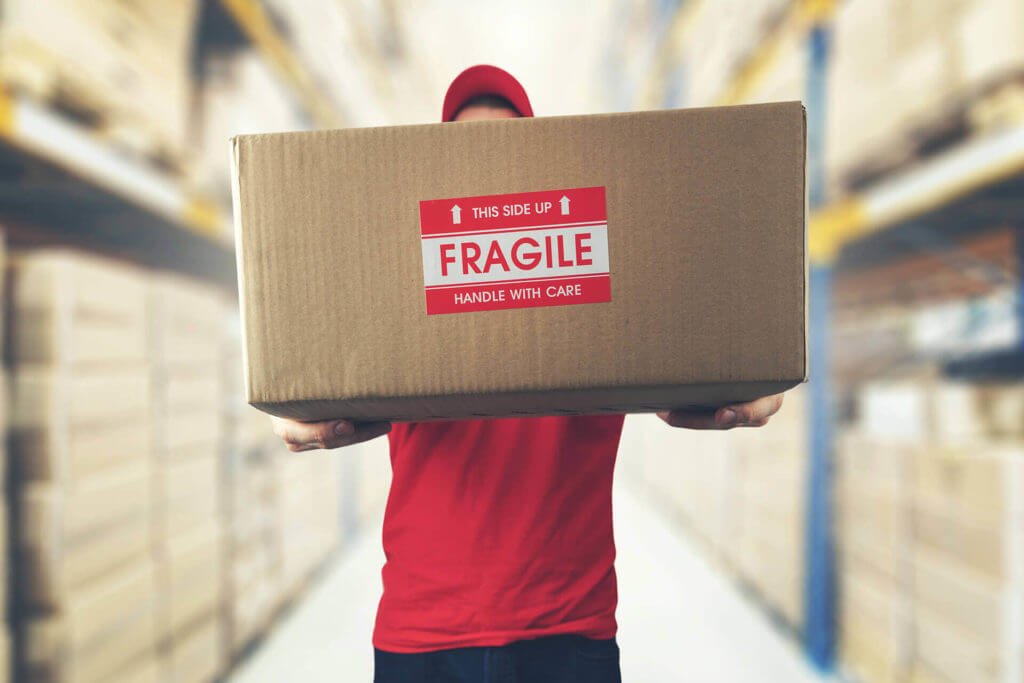 A mover holding a box with a fragile sticker on it