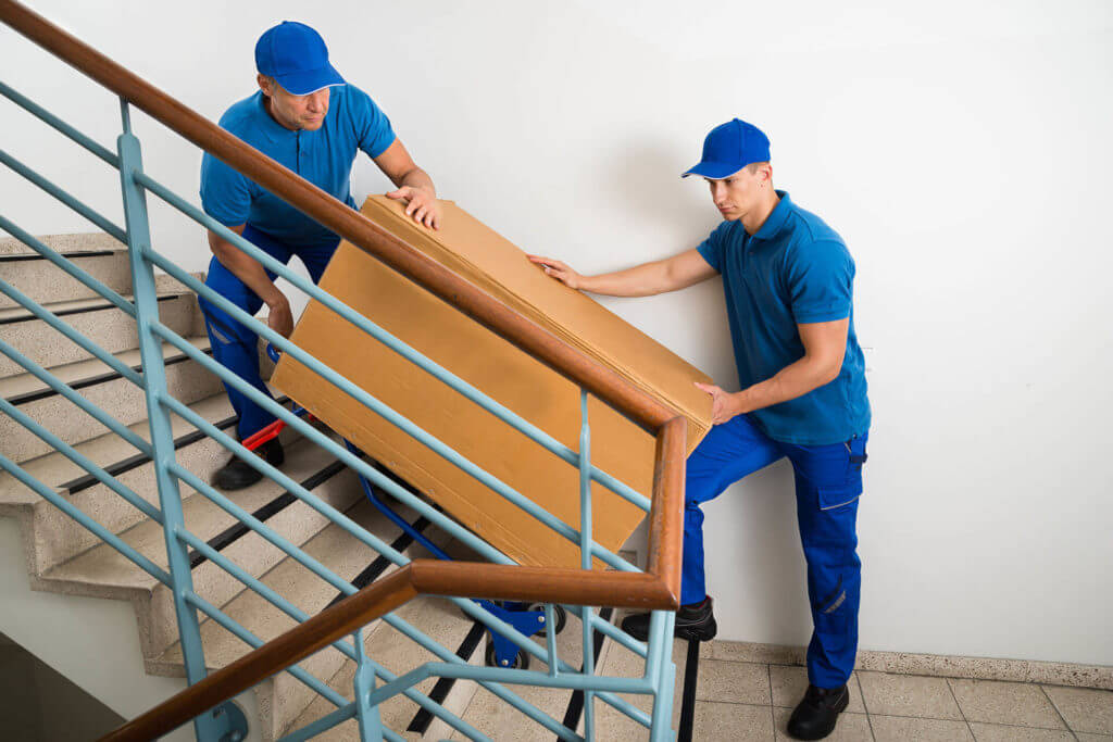 Two cross-country movers carrying furniture up some stairs