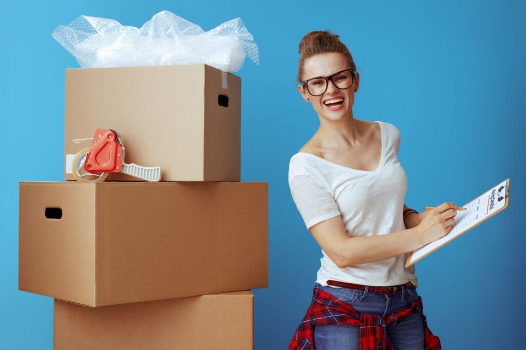 A girl near a pile of boxes writing a list for a long-distance moving company