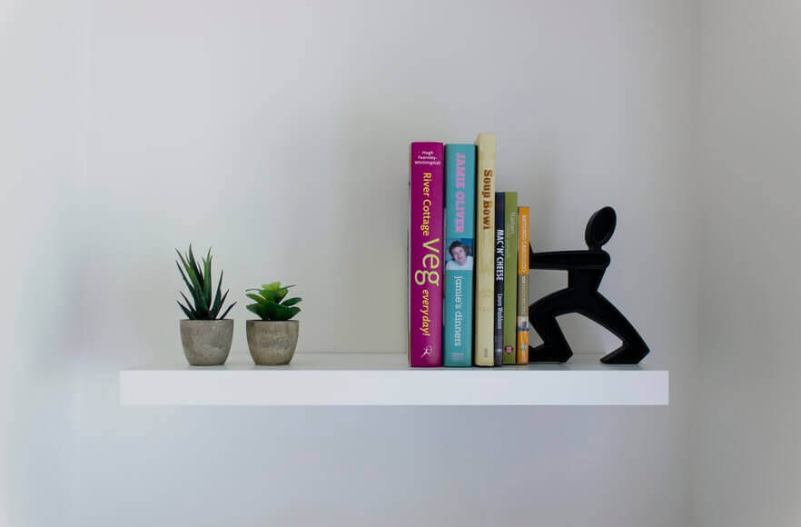 A floating shelf with books and two small plant pots