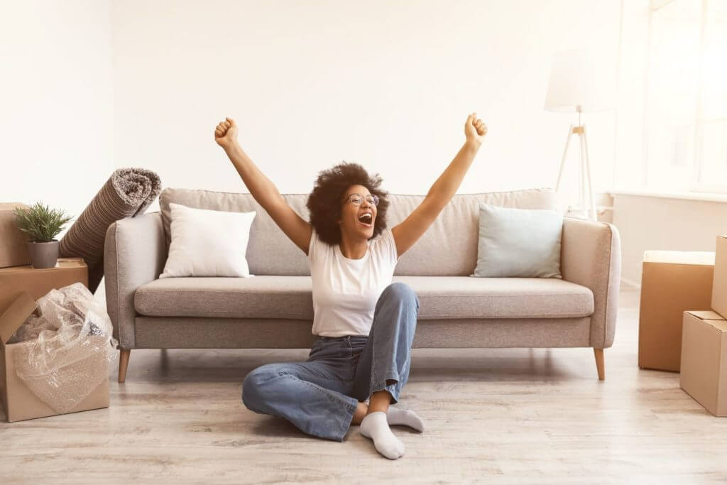 A young woman on the floor in front of the sofa, excited about her long-distance moving
