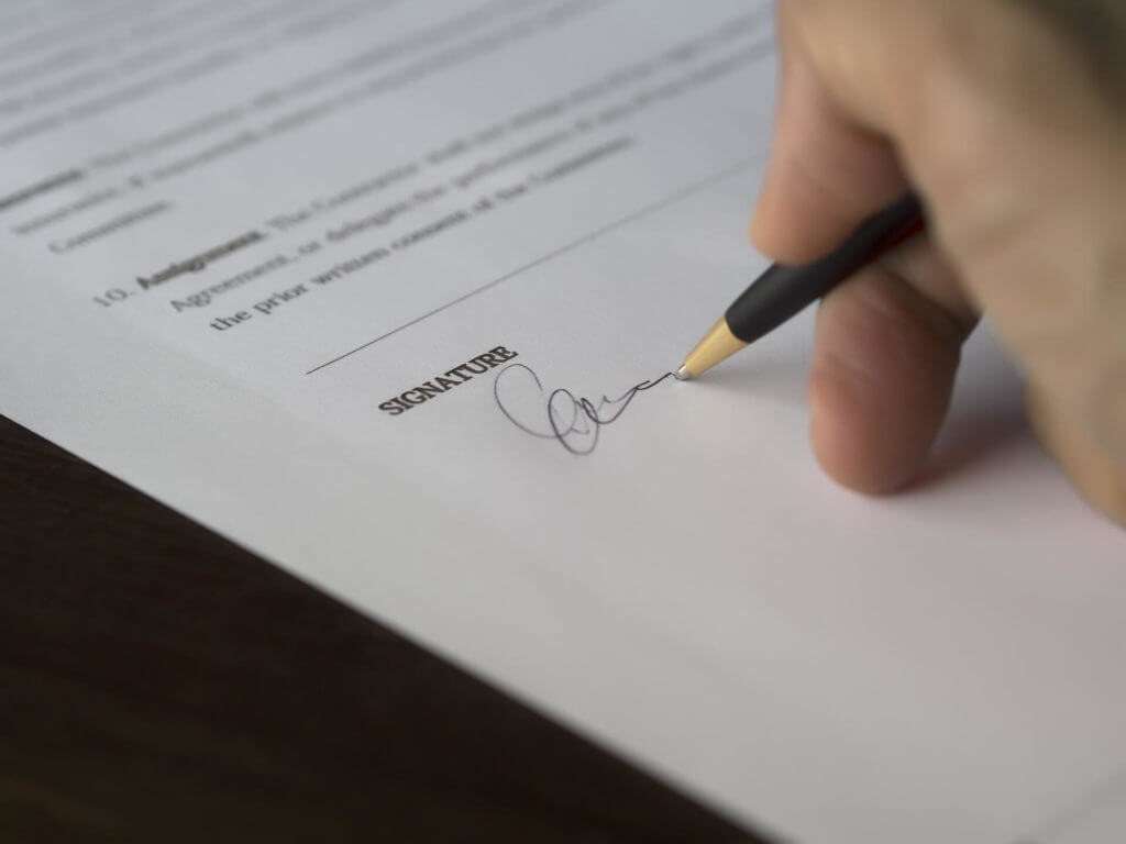 A person off-screen signing a document