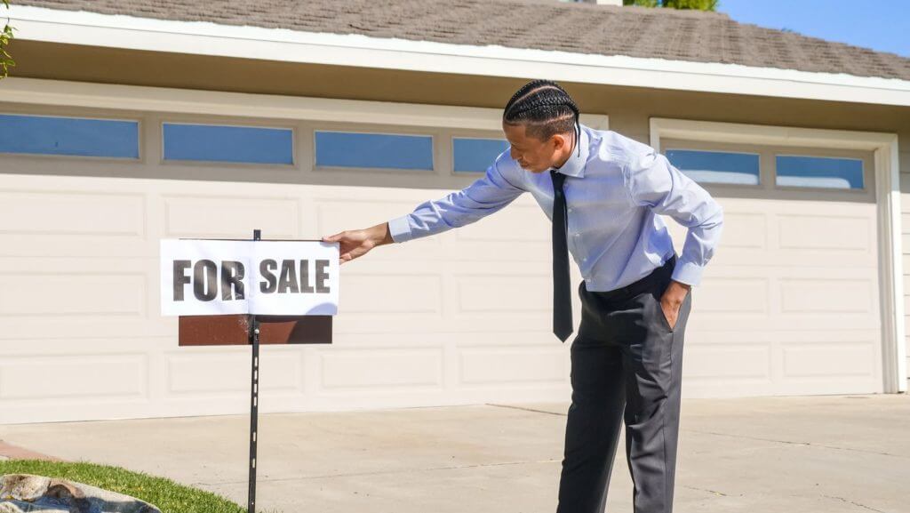 A man adjusting the “for sale” sign in front of the garage doors