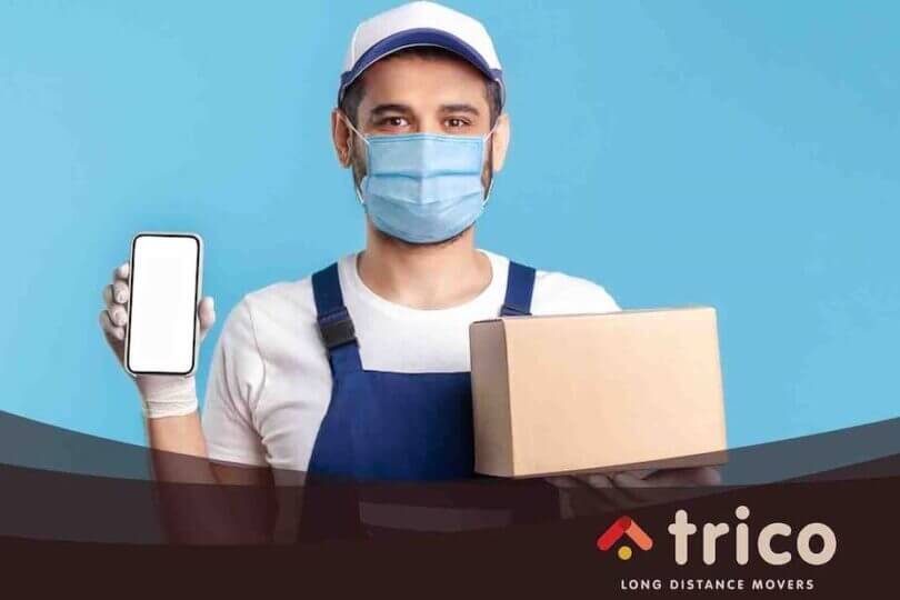 One of the long-distance movers near me with a face mask holding a smartphone and a box