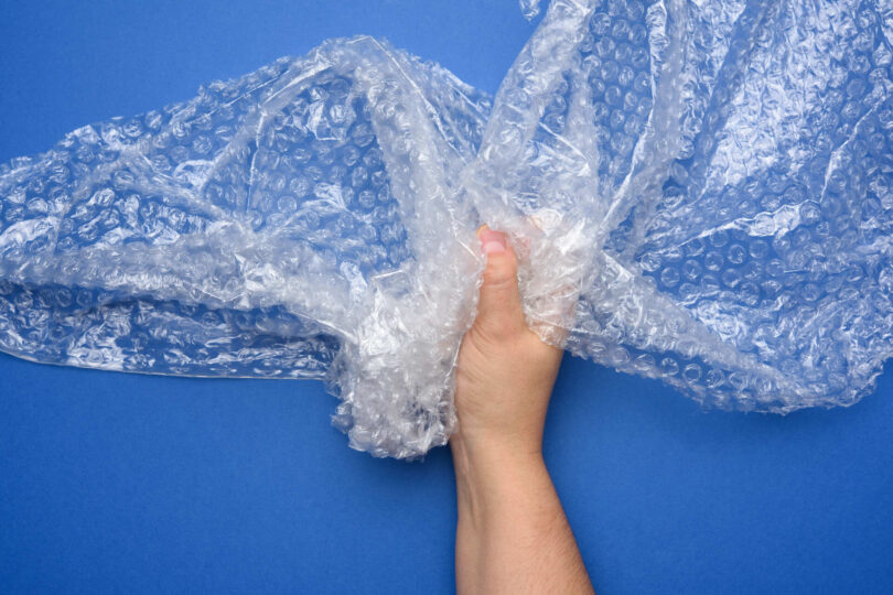 A hand holding some bubble wrap on a blue surface