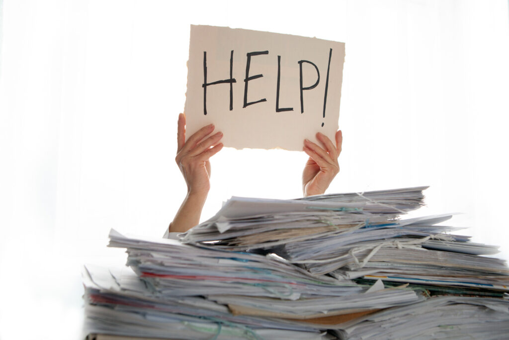 A person holding a help sign surrounded by a pile of papers
