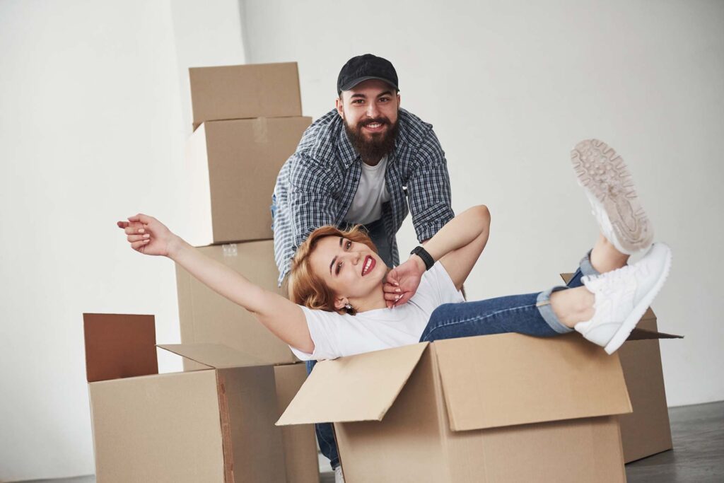 Cheerful young couple playing around and laughing inside a large cardboard box while packing up their home.