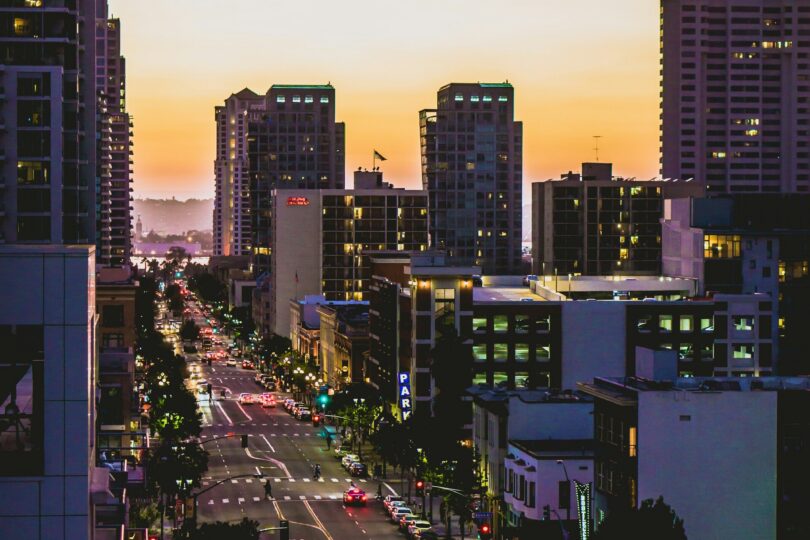 Vehicle driving on a paved road between high-rise buildings at sunset in East Village, San Diego.