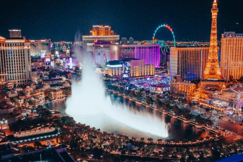 A nighttime high-angle view of the iconic Bellagio Fountains and the Las Vegas Strip surrounded by illuminated city lights.