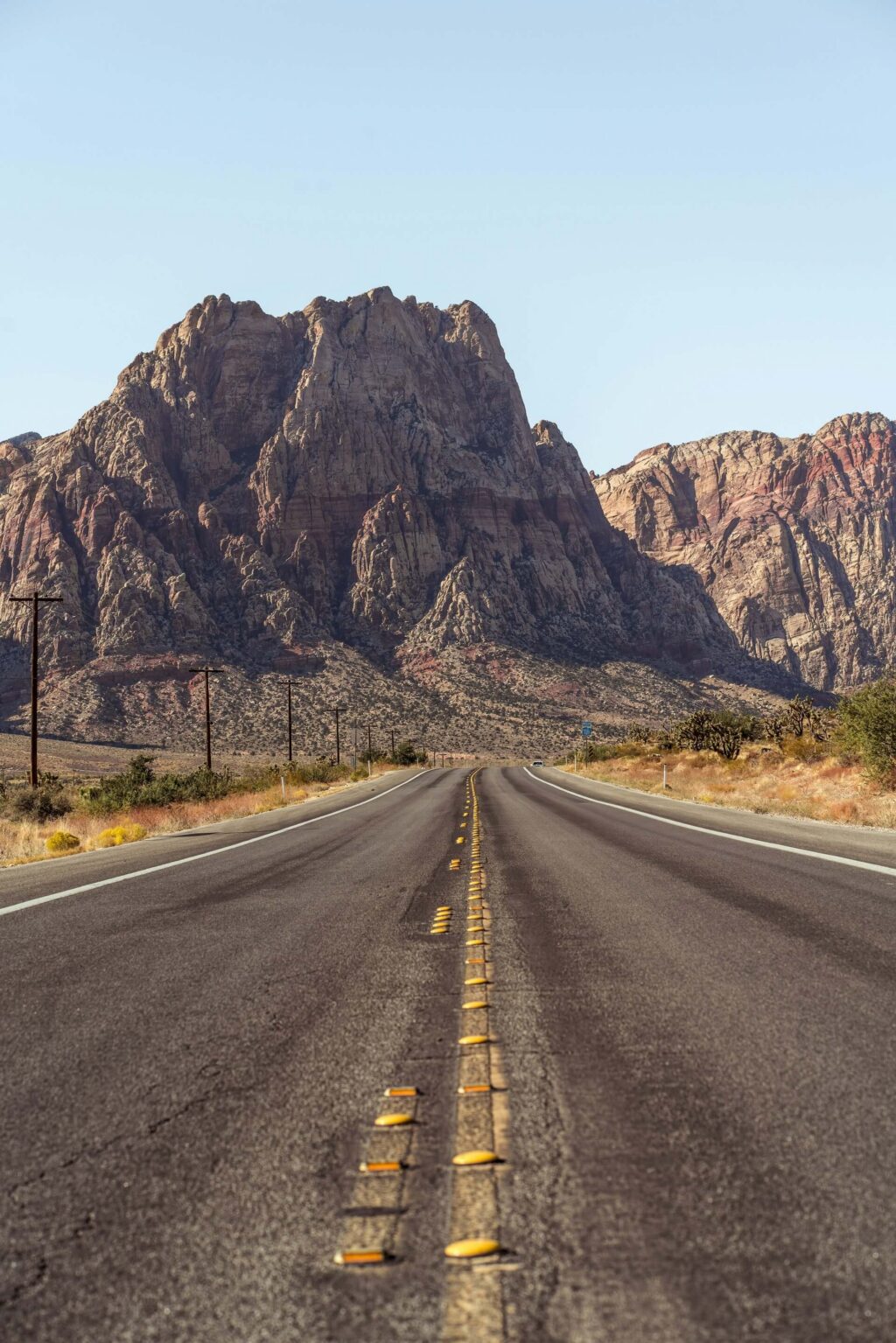 An open highway stretching toward majestic mountains in the distance under a blue sky.